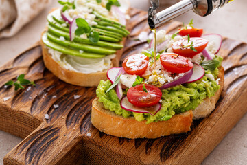 Avocado toasts with radishes, tomatoes and feta topped with olive oil