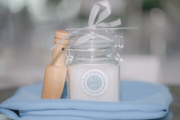Beautiful Sea Salt filled clear jar with white bow wedding favor with wood on blue blanket in front of white bokeh