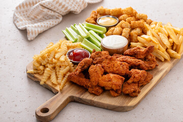 Fried chicken strips and french fries board with sauces and celery