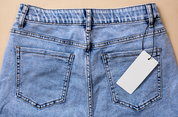 Blue jeans with a paper label on a beige background. Black Friday clothing sale. Mock up.