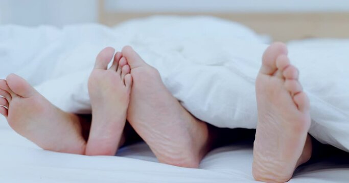 Couple, feet and together in bed on holiday, vacation or sleeping with comfort, care and love in bedroom in home. People, relax and foot or toes touching in affection under blanket in the morning