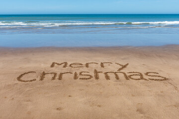 Merry Christmas text written on the sand of the beach.