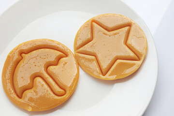Dalgona candy or Ppopgi. Sugar Honeycomb cookie with round umbrella and star shape on white plate. candy challenge