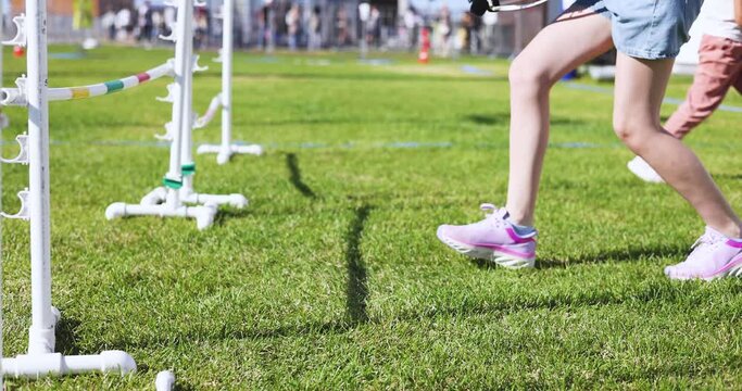 Hobby horsing competition on a green grass, hobby horse riders jumping, equestrian sport training with stick toy horses in a summer sunny day, equipment for hobbihorsing