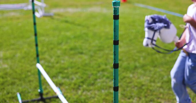 Hobby horsing competition on a green grass, hobby horse riders jumping, equestrian sport training with stick toy horses in a summer sunny day, equipment for hobbihorsing