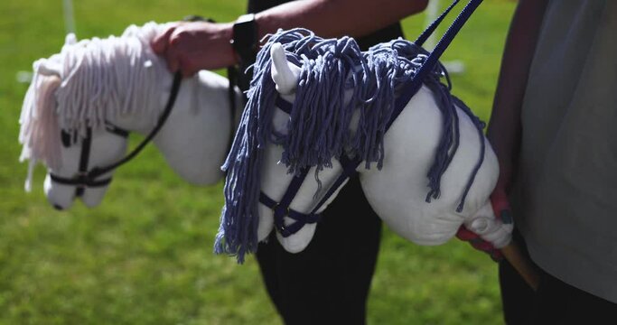 Hobby horsing competition on a green grass, hobby horse riders jumping, equestrian sport training with stick toy horses in a summer sunny day, equipment for hobbihorsing