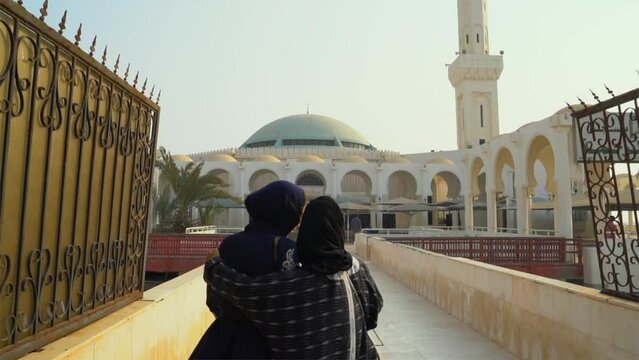 Two friends entering a Mosque near the Red Sea in Jeddah, Saudi Arabia revealing the minaret. The mosque is called "Al-Rahmah mosque, Saudi Arabia