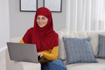 Muslim woman using laptop at couch in room. Space for text