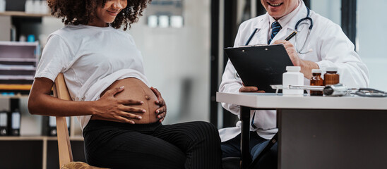 Naklejka premium Male gynecologist doctor checking african american pregnant woman, Gynecology Consultation concept, examining belly stethoscope, obstetrician OB doctor special training in women health and pregnancy