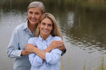 Happy mature mother and her daughter hugging near pond, space for text