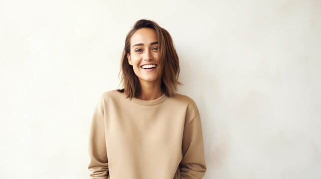   beautiful woman wearing a plain tan sweatshirt standing in front  white wall with modern decor in the background in a happy mood