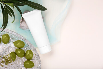 Tube of cream, olives, stone and leaves on beige background with light blue organza fabric drapery, flat lay. Space for text