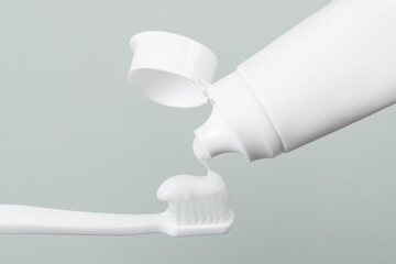 Applying paste on toothbrush against grey background, closeup
