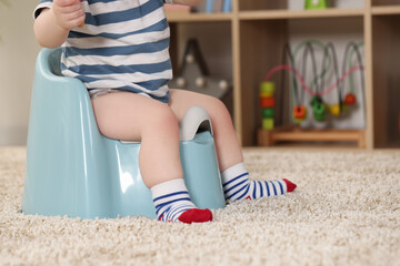 Little child sitting on plastic baby potty indoors, closeup. Space for text