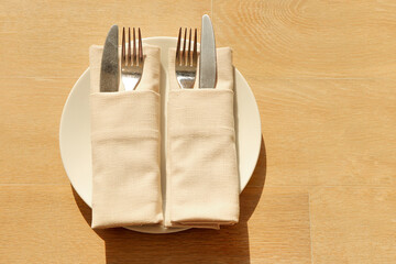 Empty white plate and silverware knife and fork on wooden background. A cloth napkin on plate with...