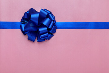 Blue ribbon with bow on pink background, top view. Space for text