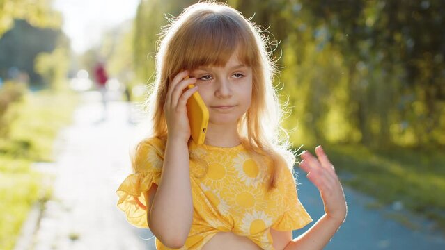 Happy preteen child kid having remote conversation communicate speaking by smartphone. Pretty blonde girl daughter talking with mother on phone good news gossip standing on city sunset park street