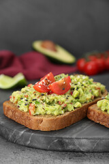 Slices of bread with tasty guacamole and ingredients on grey table, closeup