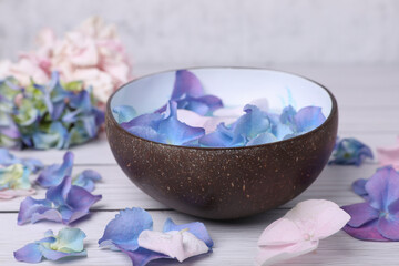 Spa composition. Aromatic water in bowl and flowers on white wooden table, closeup