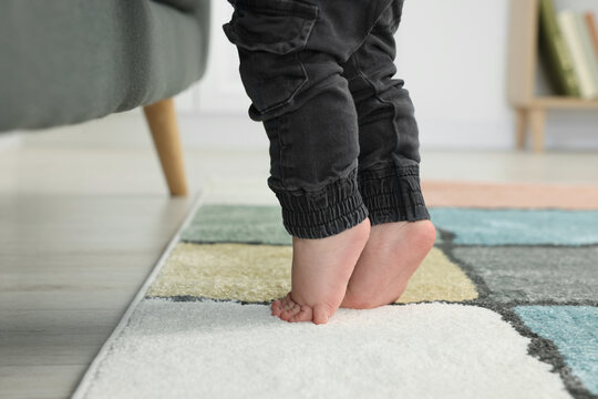 Baby standing on soft carpet near sofa, closeup