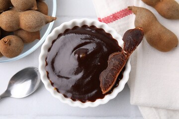 Bowl of tamarind sauce and fresh pods on white tiled table, flat lay