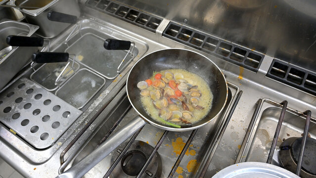 padella con pesce in cottura nella cucina di un ristorante