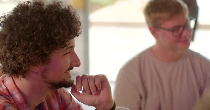 Close-up portrait of a young man nodding approvingly while actively listening to conversation partner at a table during group discussion. Agreement and approval signs. Positive conversation of people.