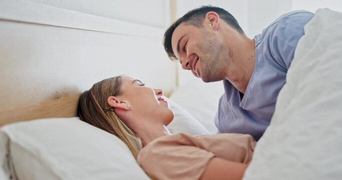 Happy, relax and couple kissing in bed while in conversation for romance or bonding together. Smile, love and young man and woman with intimate moment for resting in bedroom at home in Australia.
