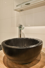 a black bowl sink on a wooden counter in a bathroom with white tile walls and wood flooring around it