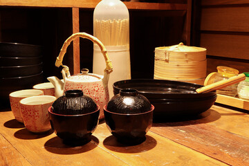 Set of black bowl with the wooden chopsticks, ceramic teapot on the wooden table in the restaurant. Japanese style tableware.