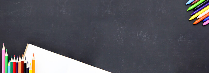 Colorful wooden pencils, notepads on blank black chalkboard. Top view with copy space. Back to school concept. Place for text and design for long web banner.