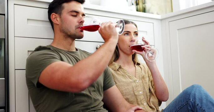 Couple on floor drinking red wine, cheers and smile to celebrate love, marriage and happy home. Toast with alcohol in glass, man and woman on ground to relax for conversation in kitchen together.