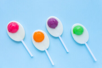 Colorful lollipops, duck egg shaped candies on sticks on light blue background. Flat lay, top view