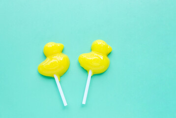 Bright yellow duck shaped candies on sticks on light green background. Duck Lollipop, Flat lay, top view