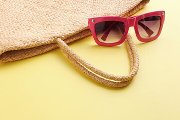 Brown wicker woven bag or straw bag and sunglasses on yellow background. Top view with copy space. Summer travel concept. 