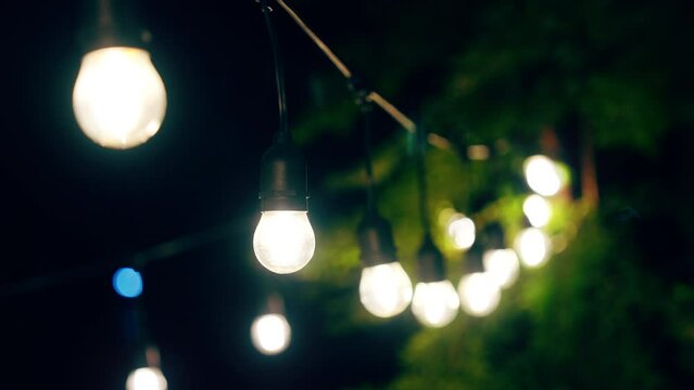 Outdoor string lights hanging on a line on outside house in backyard. Garden decoration. Party camping