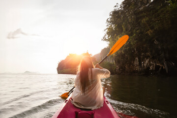 Woman kayaking on the sea with sunset over mountain. Asian woman rowing on the river. Summer travel on the beach.