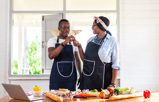 Portrait Of Love African American Couple Having Fun Cooking Together And Looking For Recipe On Internet With Laptop Computer To Prepare The Yummy Eating In Kitchen At Home