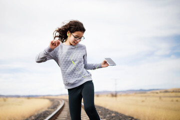 young girl with glasses listens musics  and dances on a railway, kids and technology concept