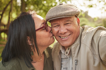 Selfie, kiss and senior couple in a park happy, bond and having fun in nature together. Portrait, love and elderly man with old woman in forest smile for profile picture, kissing and enjoy retirement