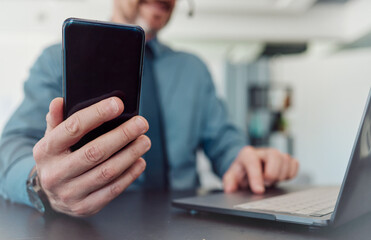 Businessman, hands and phone with laptop in communication, social media or networking at the office. Closeup of man working on computer and mobile smartphone technology in telemarketing at workplace