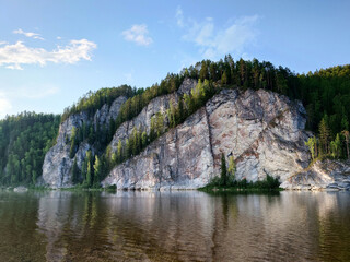 Landscape with the image of a mountain lake in the forest. The picturesque cliffs on the river bank