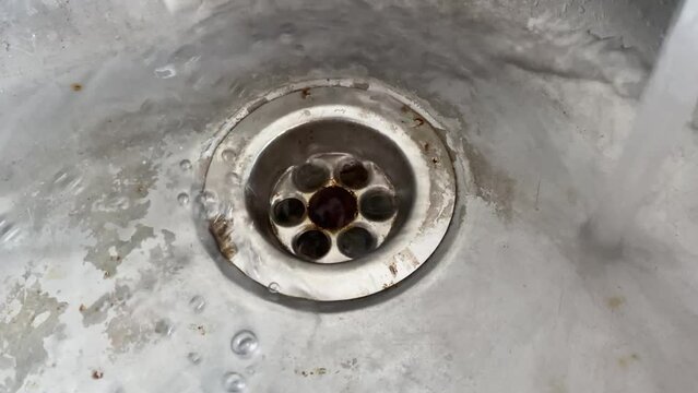 Water flowing into dirty mesh drain kitchen sink holes close up view