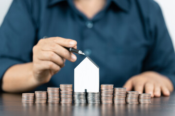 Saving money for house and real estate. Woman hand pointing on stack coins and house model on table.