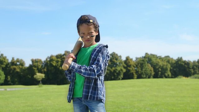 Portrait of serious lovely school age African American boy baseball hitter with baseball bat wearing eye black, ready to hit a shot and waiting for pitch while enjoying playing game on green field.