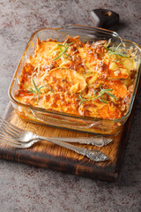 Vegetarian sweet potato gratin with cheddar cheese and rosemary close-up in a glass form on the table. Vertical