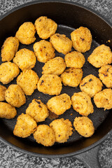 Spicy coated southern fried chicken bites in a cast iron frying pan. On a black granite background