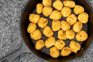 Spicy coated southern fried chicken bites in a cast iron frying pan. On a black granite background