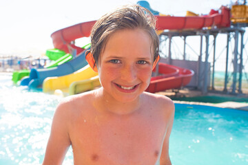 happy 10 year old boy in water amusement park spends summer holidays. joyful smiling wet child...