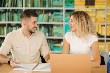 Portrait of boy and girl study in public library. Female using laptop and boy write something in notebook 